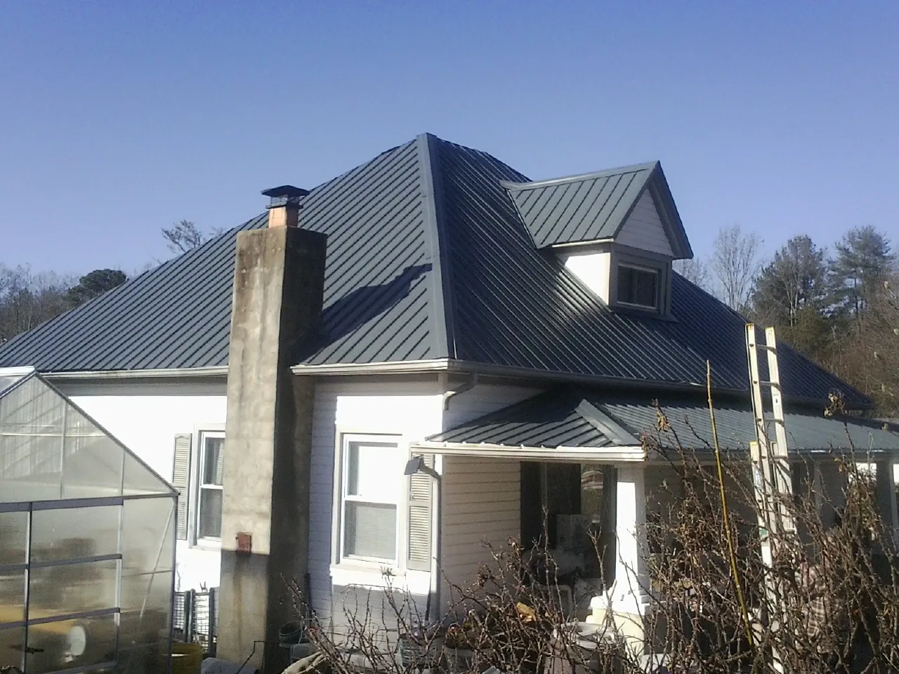 Dark blue standing seam metal roof on a white farmhouse with dormer — Slate & Tile Roof Repair by Roofing Brothers in Atwater
