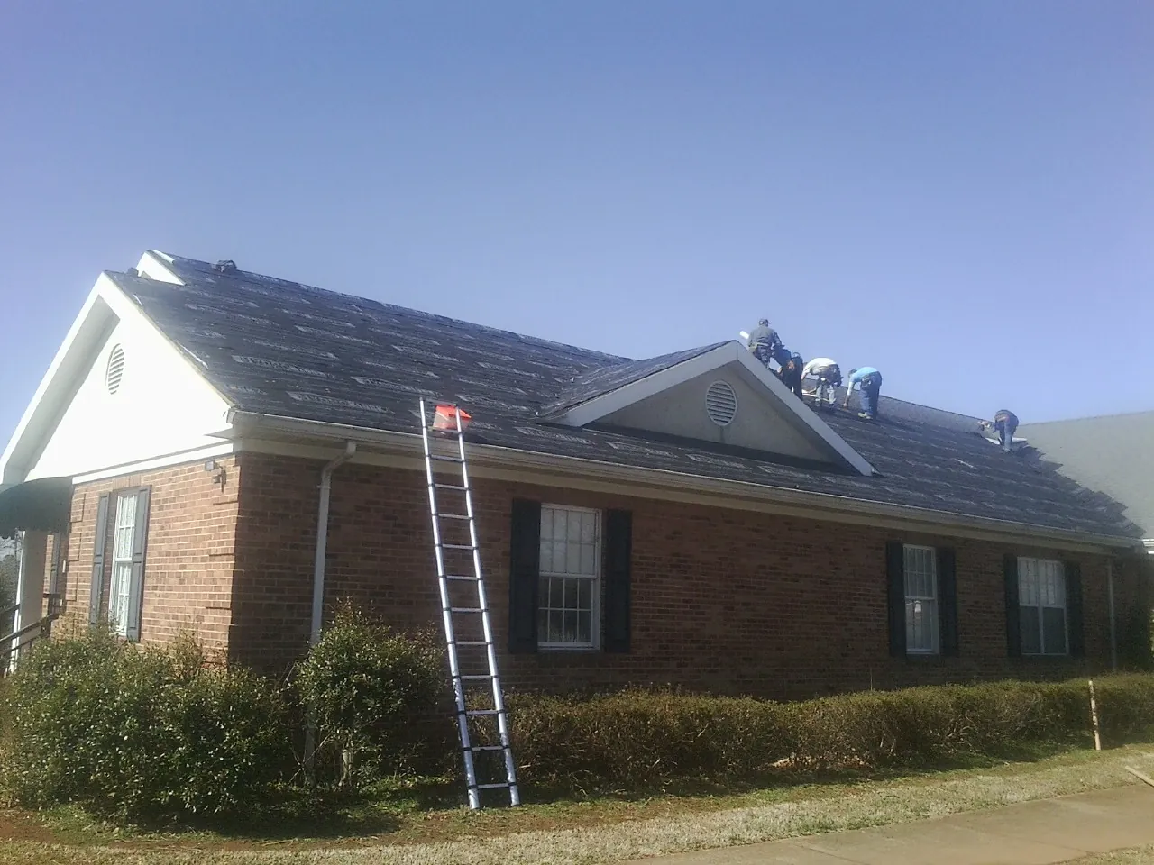 Crew tearing shingles off a brick ranch roof with a ladder set — Emergency Roof Repair work by our crew in Atwater