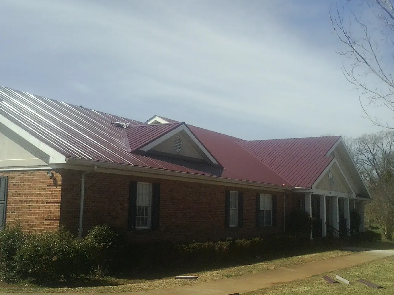 Red metal roof with gabled entries on a long brick building, from a Hail Damage Roof Repair job in Atwater