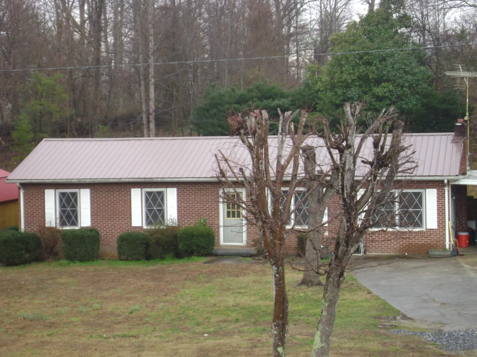 Mauve metal roof on a brick ranch home behind bare trees in Atwater