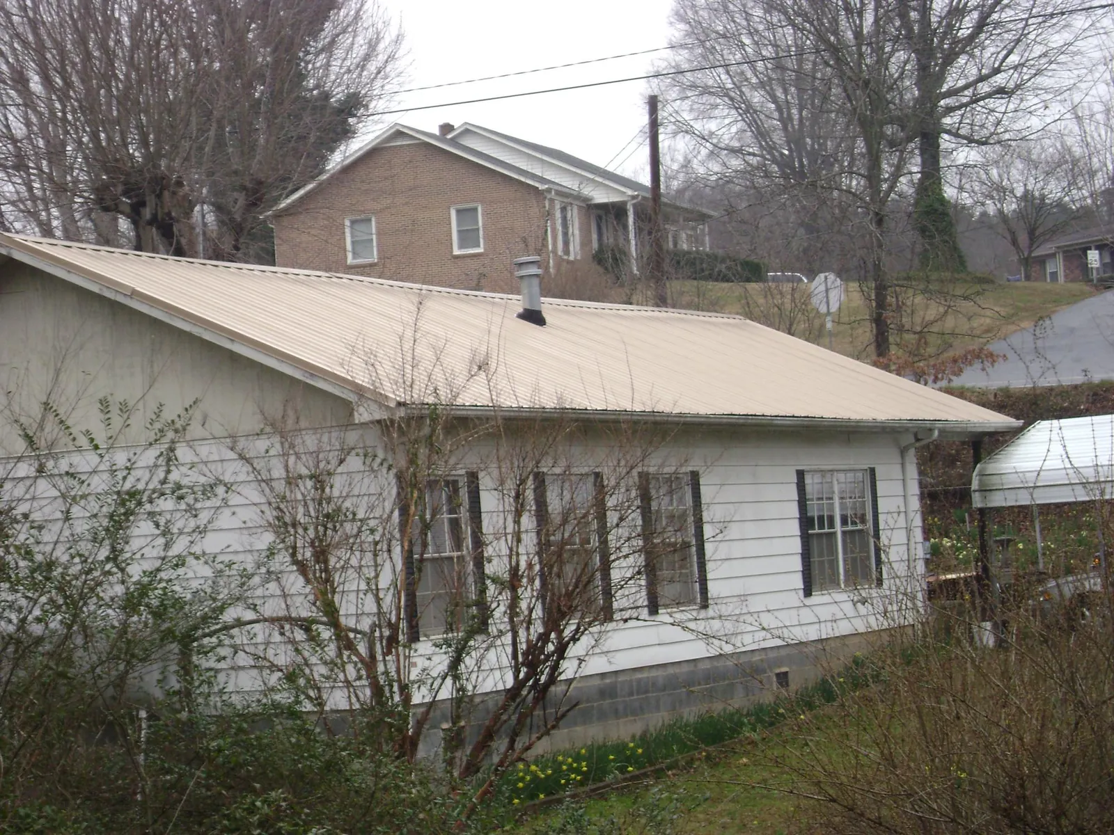 Tan metal roof on a white sided house set into a hillside — Commercial Roofing by Roofing Brothers in Atwater
